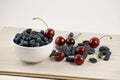 Fresh ripe honeysuckle berries and cherry in a ceramic bowl on a wooden board. Healthy breakfast. White bowl of honeysuckle. Royalty Free Stock Photo