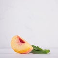 Fresh ripe juicy piece peach and green leaf on white wood board, square.