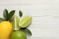 Fresh ripe lemon, limes and green leaves on white wooden background, flat lay. Space for text Royalty Free Stock Photo