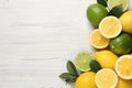 Fresh ripe lemons, limes and green leaves on white wooden background, flat lay. Space for text Royalty Free Stock Photo