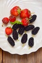 Fresh ripe mulberries with mint and strawberries in white bowl