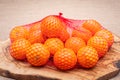 Fresh ripe organic mandarins in plastic mesh sack on olive wood and burlap