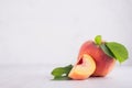 Fresh ripe peach with juicy piece and green leaf on white wood board, copy space.