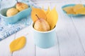 Fresh ripe pear and yellow autumn leaves in enameled cup on a white background. Copy space Royalty Free Stock Photo