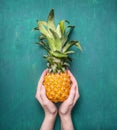 Fresh ripe pineapple small, in the hands of girl on the turquoise wooden background