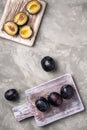 Fresh ripe plum fruits whole and sliced on wooden cutting boards, stone concrete background, top view Royalty Free Stock Photo