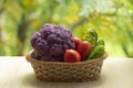 Fresh ripe purple cauliflower, red tomatoes and green cucumber in basket. Healthy food on table on defocus autumn