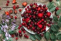 Fresh ripe red berries - cherry, strawberry and raspberry on a plate with summer flowers on rustic wooden background Royalty Free Stock Photo