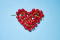 Fresh ripe red cherries arranged in a heart shape on the blue background