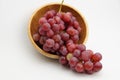 Fresh and ripe red grapes in a wooden bowl, isolated in white background. Bunch of raw and juicy grapevines