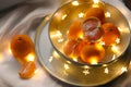 Fresh ripe tangerines and glowing fairy lights on white cloth, above view