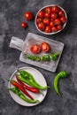 Fresh ripe tomatoes in bowl near to old wooden cutting board with hot chili peppers in plate Royalty Free Stock Photo