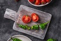 Fresh ripe tomatoes in bowl near to old wooden cutting board with hot chili peppers in plate, dark stone concrete background Royalty Free Stock Photo