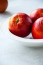 Fresh ripe whole and slices of blood oranges in a plate on a white stone background. Copy space and close up. Royalty Free Stock Photo