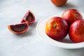 Fresh ripe whole and slices of blood oranges in a plate on a white stone background. Copy space and close up. Royalty Free Stock Photo