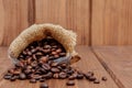 Fresh roasted coffee beans falling out the sack on the wooden surface. Brown coffee beans scattered from bag on the table Royalty Free Stock Photo