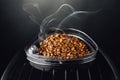 Fresh roasted coffee beans with smoke in coffeemaker bean container, close-up view