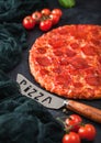 Fresh round baked Hot and Spicy Pepperoni pizza with knife and tomatoes with basil on black background with kitchen cloth. Close Royalty Free Stock Photo