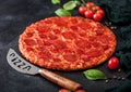 Fresh round baked Hot and Spicy Pepperoni pizza with knife and tomatoes with basil on black background with kitchen cloth. Close Royalty Free Stock Photo