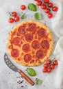 Fresh round baked Pepperoni italian pizza with knife with tomatoes and basil on light background with linen towel. Top view Royalty Free Stock Photo