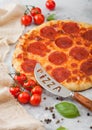 Fresh round baked Pepperoni italian pizza with knife with tomatoes and basil on light background with linen towel. Top view Royalty Free Stock Photo