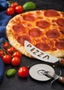 Fresh round baked Pepperoni italian pizza with wheel cutter and knife with tomatoes and basil on black background. Close up Royalty Free Stock Photo