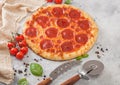 Fresh round baked Pepperoni italian pizza with wheel cutter and knife with tomatoes and basil on light background with linen towel Royalty Free Stock Photo