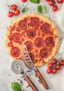 Fresh round baked Pepperoni italian pizza with wheel cutter and knife with tomatoes and basil on light background with linen towel Royalty Free Stock Photo