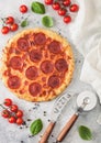 Fresh round baked Pepperoni italian pizza with wheel cutter and knife with tomatoes and basil on light background with linen towel Royalty Free Stock Photo
