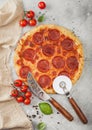 Fresh round baked Pepperoni italian pizza with wheel cutter and knife with tomatoes and basil on light background with linen towel Royalty Free Stock Photo