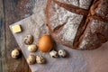 Fresh round homemade rye bread wrapped in baking paper, colored chicken and quail eggs, a slice of cheese Royalty Free Stock Photo