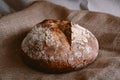 Fresh round loaf of healthy whole grain bread on brown jute burlap fabric background with white flour on top. top view of homemade Royalty Free Stock Photo