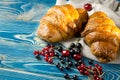 Fresh ruddy croissants with berries lie on a wooden table next to fresh black currant berries, red currants, cherries