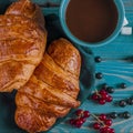 Fresh ruddy croissants with berries lie on a wooden table next to fresh black currant berries, red currants Royalty Free Stock Photo