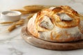 a fresh ruddy round loaf of bread lying on a wooden stand on a marble background next to wheat ears,the concept of a bakery Royalty Free Stock Photo