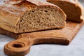 Fresh rye bread loaf on a wooden chopping board over white textured background, shallow depth of field Royalty Free Stock Photo