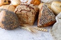 Fresh rye wheat loaf bread, various buns with seeds grains and ears closeup on rustic table Royalty Free Stock Photo