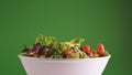 Fresh salad falling in bowl on green background, 240 fps slow motion