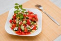 Fresh salad of finely chopped cucumbers, tomatoes and onions with sunflower oil in a white plate and a fork on a wooden table. Royalty Free Stock Photo