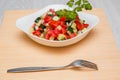 Fresh salad of finely chopped cucumbers, tomatoes and onions with sunflower oil in a white plate and a fork on a wooden table. Royalty Free Stock Photo