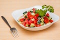 Fresh salad of finely chopped cucumbers, tomatoes and onions with sunflower oil in a white plate and a fork on a wooden table. Royalty Free Stock Photo