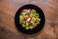 Fresh salad with fish, arugula, eggs,red pepper, lettuce, fresh sald leaves and tomato on a black plate on wooden table Royalty Free Stock Photo