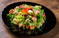 Fresh salad with fish, arugula, eggs,red pepper, lettuce, fresh sald leaves and tomato on a black plate on wooden table Royalty Free Stock Photo