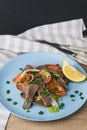 Fresh salad with pork heart, lettuce, tomato, green onion and lemon in blue plate on wooden table Royalty Free Stock Photo