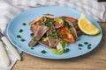 Fresh salad with pork heart, lettuce, tomato, green onion and lemon in blue plate on wooden table Royalty Free Stock Photo