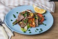 Fresh salad with pork heart, lettuce, tomato, green onion and lemon in blue plate on wooden table Royalty Free Stock Photo