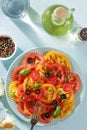 Fresh salad of red and yellow tomato slices on the plate on pastel blue background.