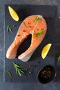 Fresh salmon steak with ingredients for cooking on a board on dark background. Raw trout steak with salt, pepper, lemon and Royalty Free Stock Photo