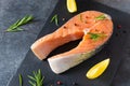 Fresh salmon steak with ingredients for cooking on a board on dark background. Raw trout steak with salt, pepper, lemon and Royalty Free Stock Photo