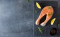 Fresh salmon steak with ingredients for cooking on a board on dark background. Raw trout steak with salt, pepper, lemon and Royalty Free Stock Photo